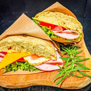 Breakfast ciabatta cut in half, filled with salad, cheese, ham and egg, on a wooden board