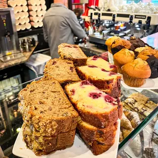 The cake cabinet stacked with muffins, slices and traybakes, a barista working behind it