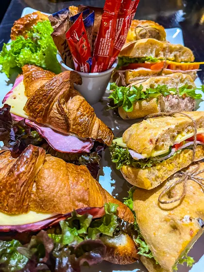 A platter of ham and cheese croissants and ciabattas tied with string, with a cup of ketchup sachets