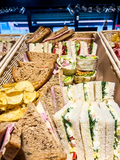 Two wicker baskets of sandwiches on wholemeal and white bread, wraps and bags of crisps
