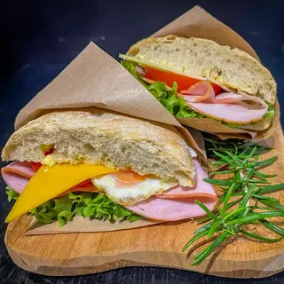 Two ciabattas with ham, cheese, egg and salad, wrapped in paper on a wooden board