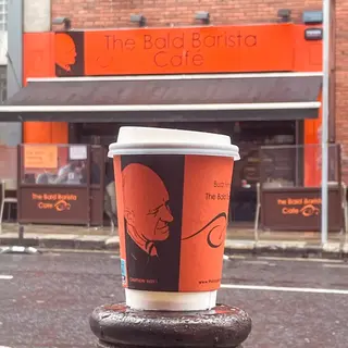 A takeaway cup printed with Buzz's face held up in front of the red café sign