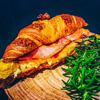 A golden croissant filled with scrambled eggs and crispy bacon