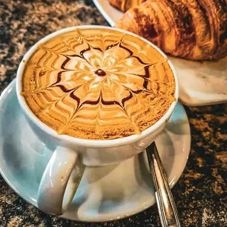 A latte with a rosetta poured into the foam, served beside a croissant
