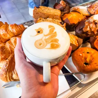 A cappuccino with a swan poured into the foam, held up in front of the pastry cabinet