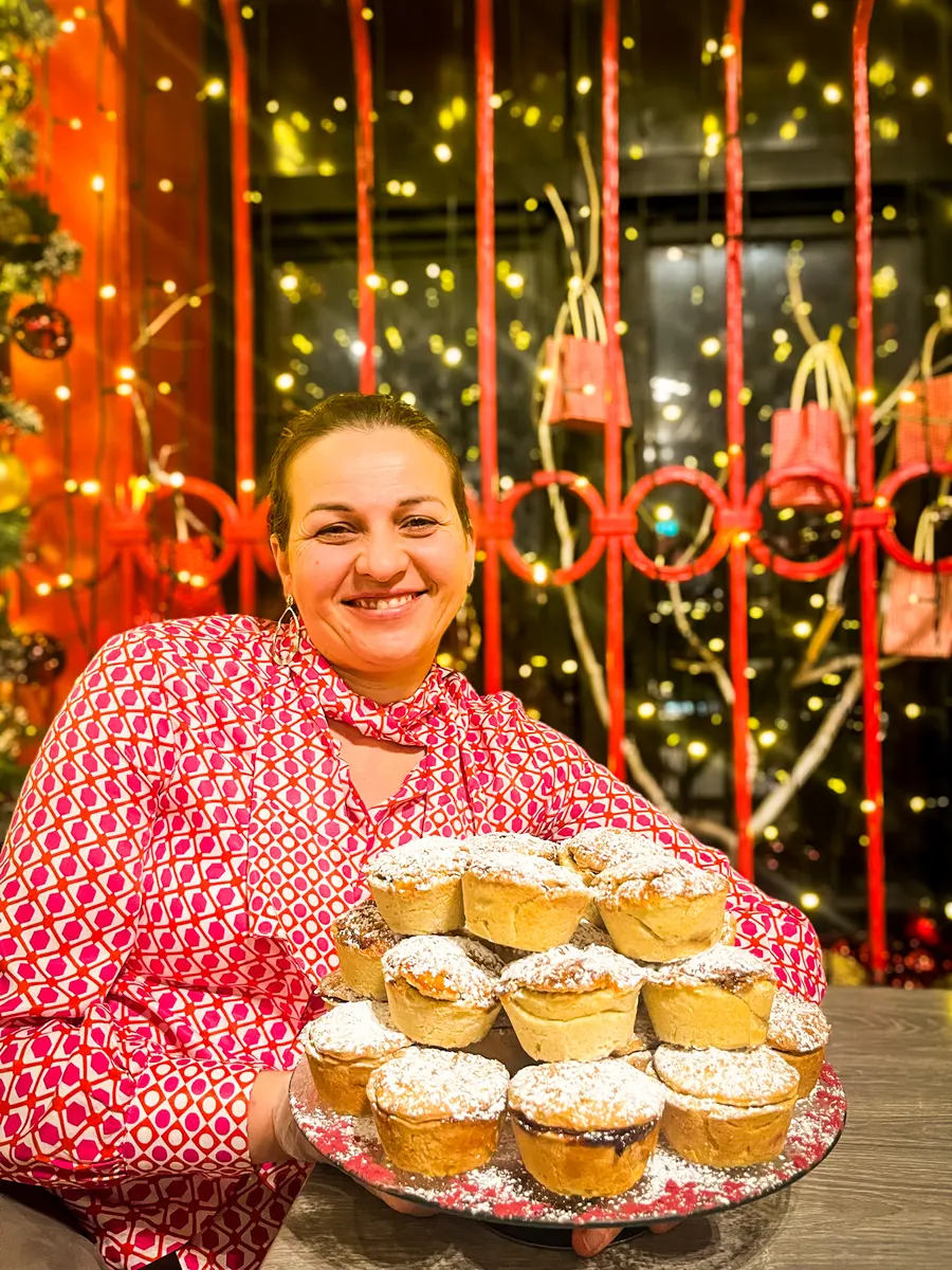 Monika smiling behind a tiered plate of mince pies dusted with icing sugar