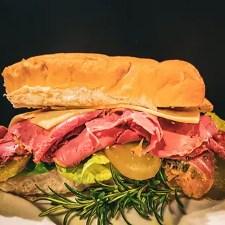 A roast beef sandwich with pickles, cut and served on a board