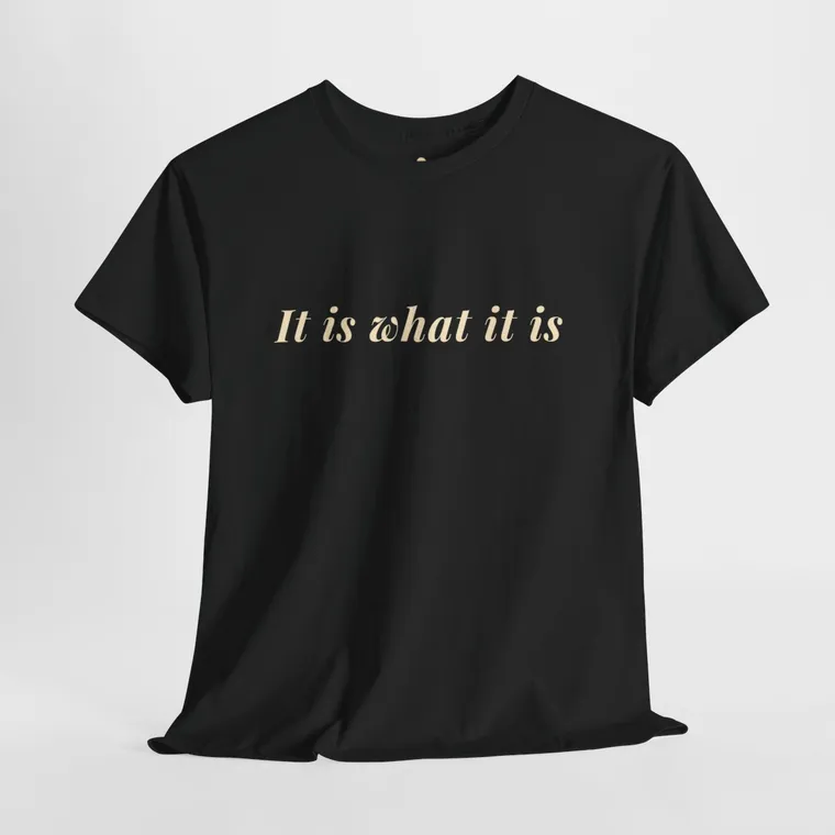 Black T-shirt laid flat with the words It is what it is printed across the chest in cream italics