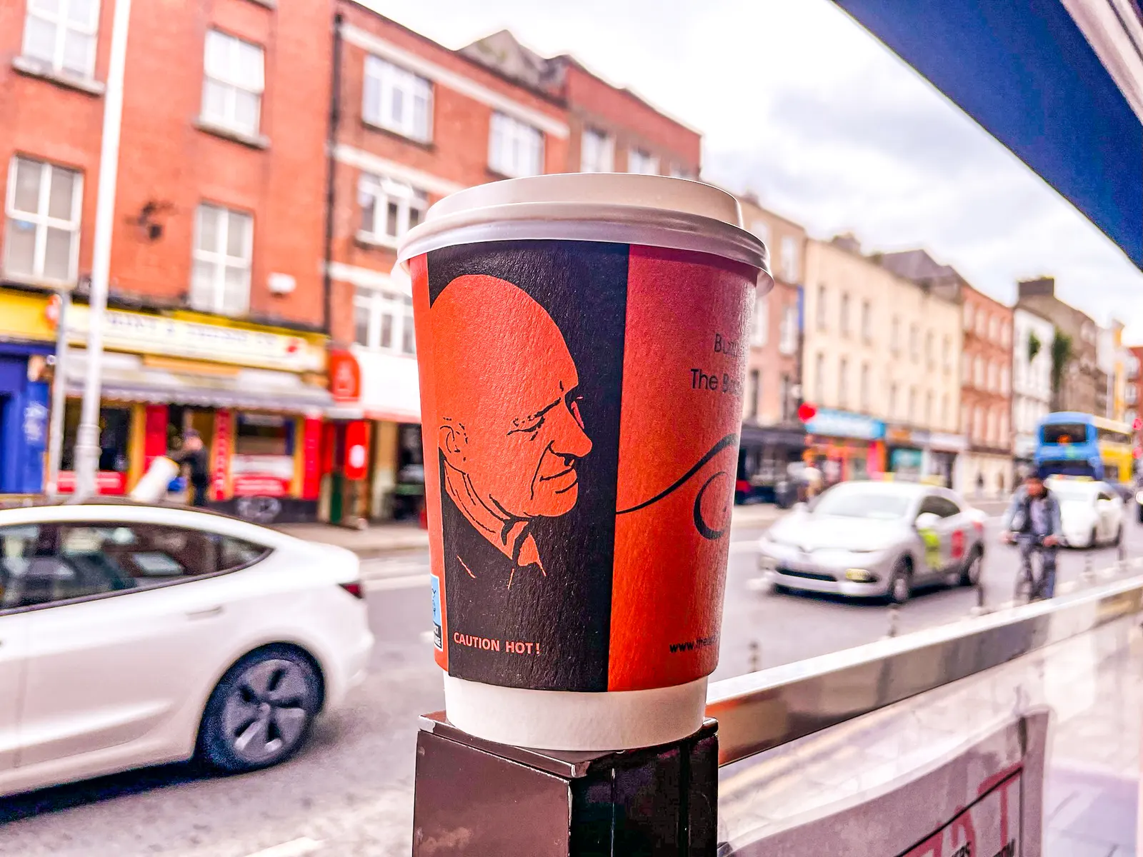A takeaway cup on the café window ledge with Dublin traffic passing on Aungier Street behind